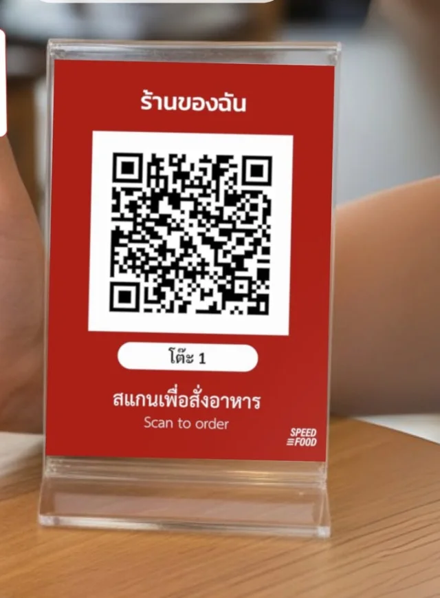 ป้าย QR ตั้งโต๊ะของ Speed Food เขียนว่าสแกนเพื่อสั่งอาหาร วางอยู่บนโต๊ะไม้ในร้าน